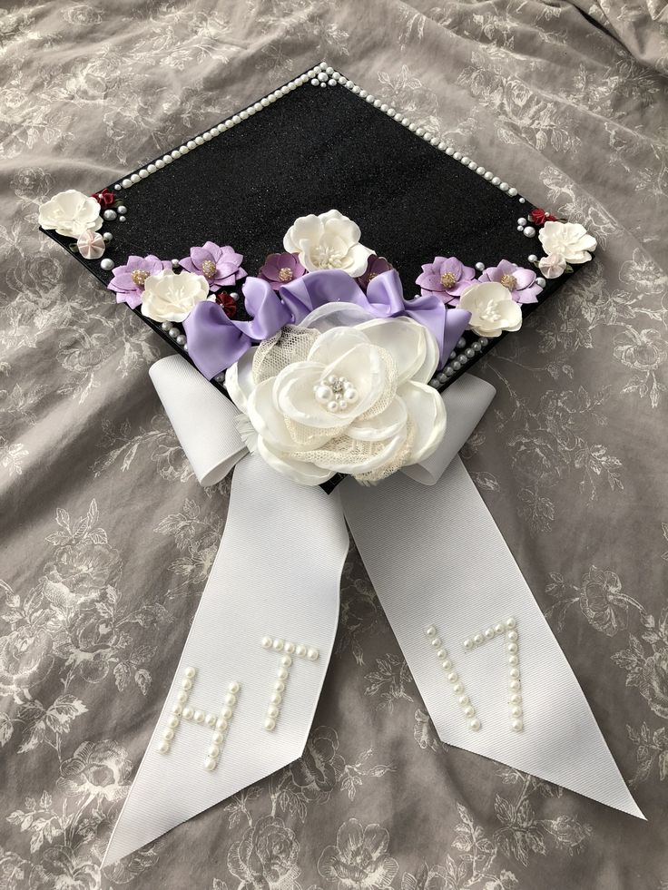 a graduation cap decorated with flowers and ribbons on a bed sheet in front of a pillow