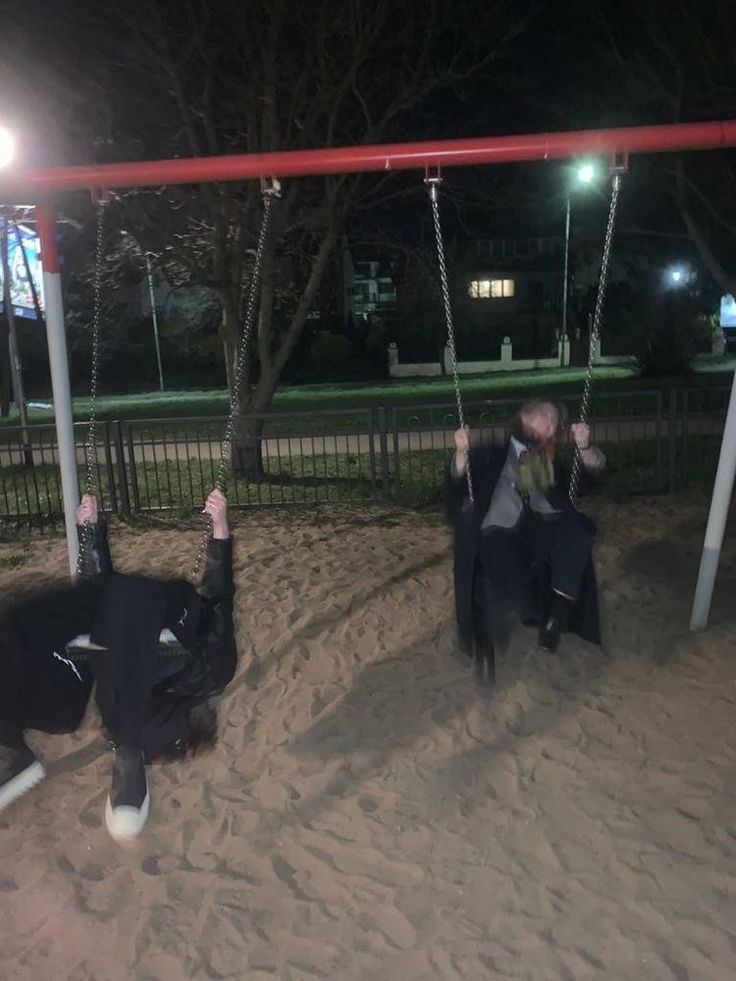 two people sitting on swings in the sand at night, with one person upside down