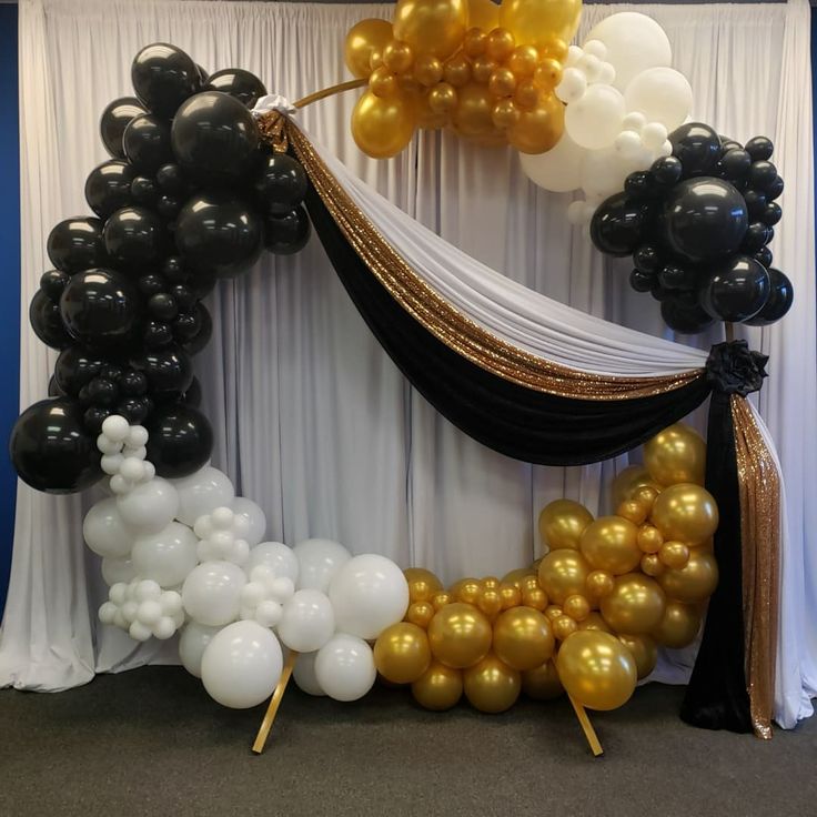 black and gold balloons are hanging on the wall in front of a white drape