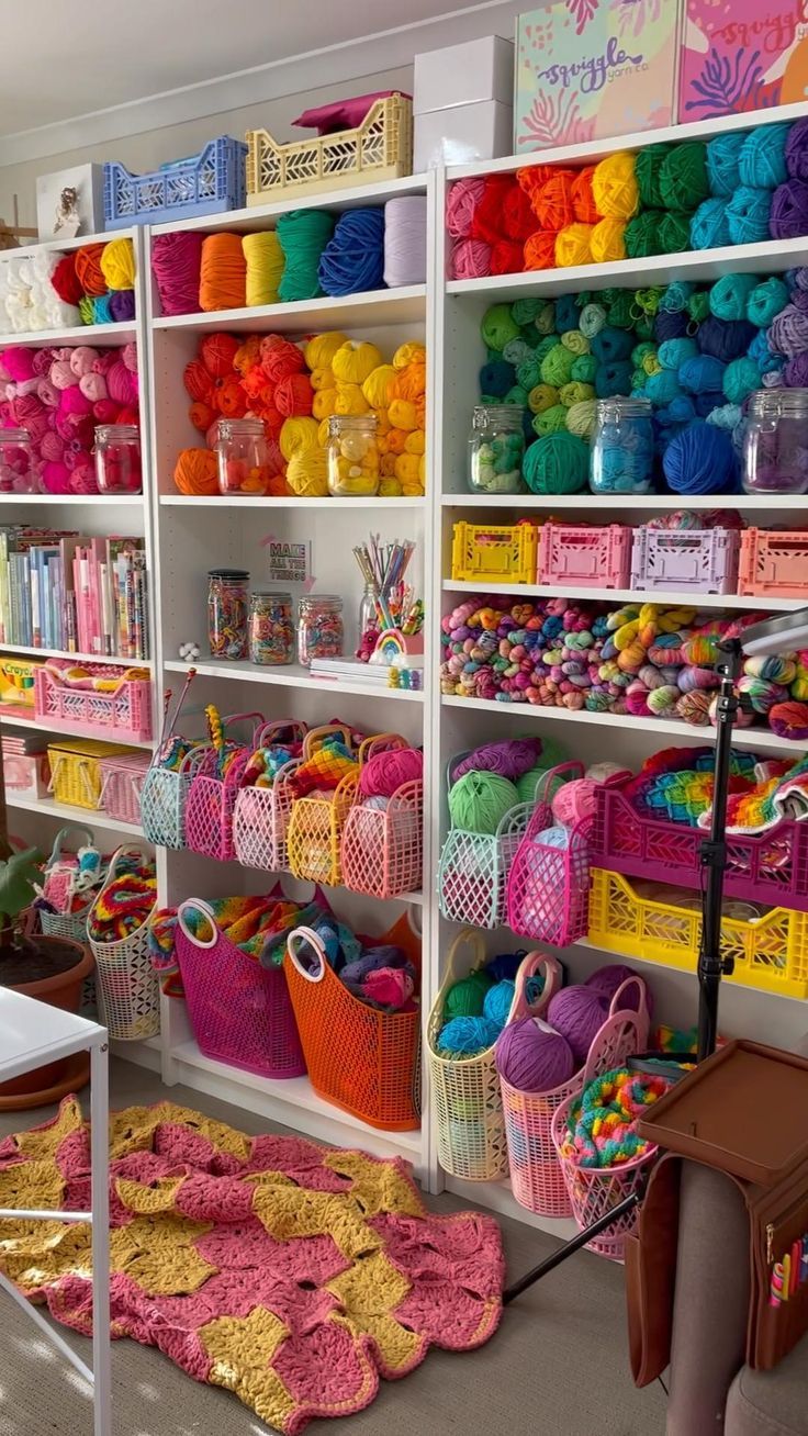 a room filled with lots of colorful yarn and crochet baskets next to white shelving