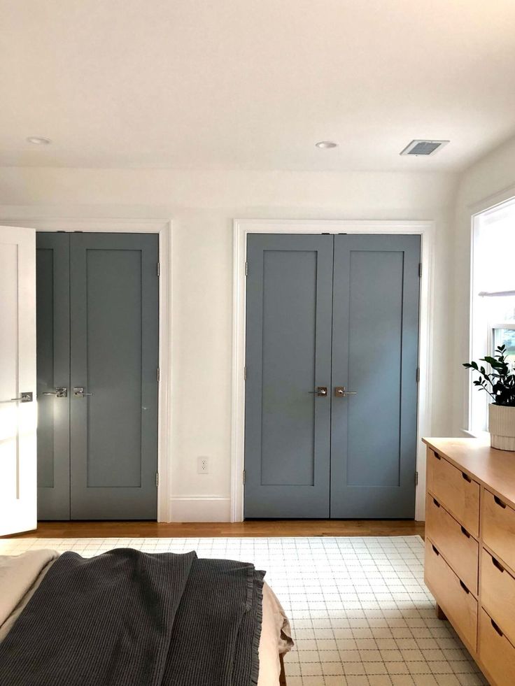 an empty bedroom with two blue doors and a bed in the foreground is shown