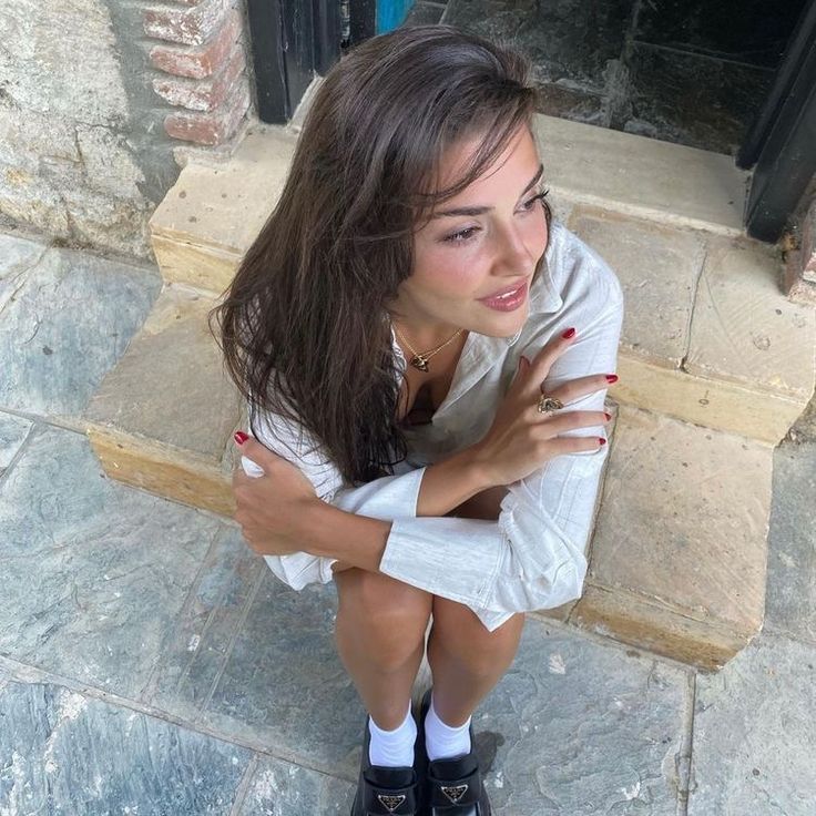 a young woman sitting on the ground with her arms crossed and looking at the camera