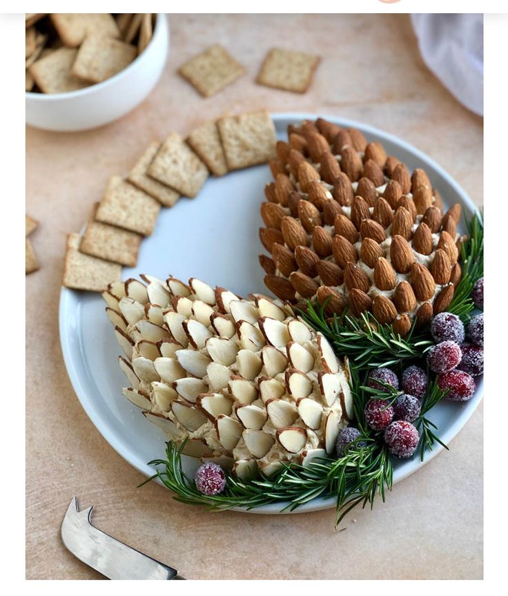 a white plate topped with pine cones and crackers next to a bowl of cranberries