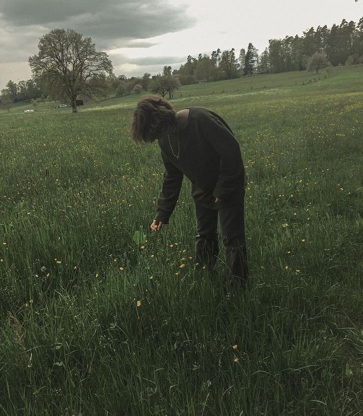 a woman is in the middle of a grassy field, picking something up with her hands