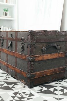 an old trunk sitting on top of a black and white checkered floor next to a window