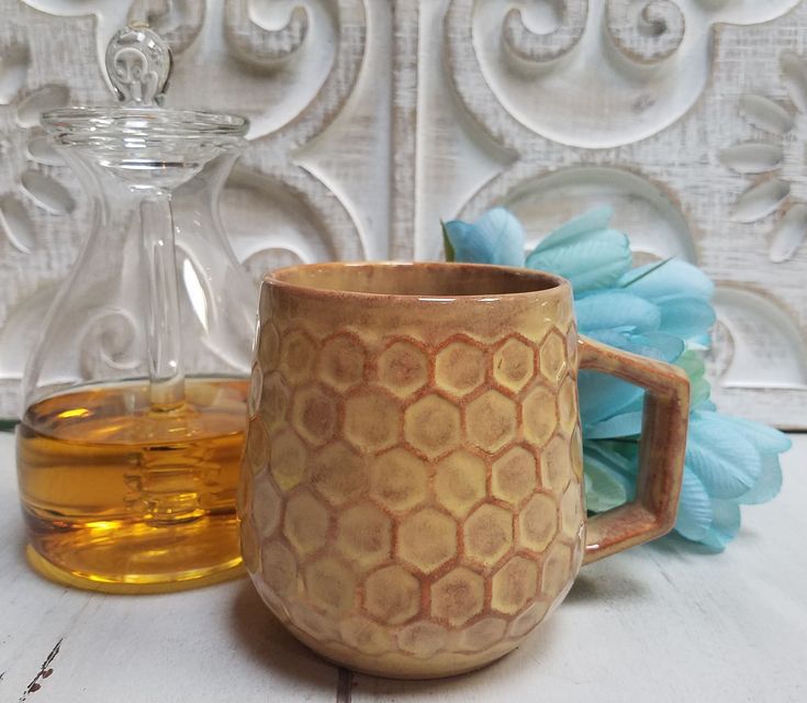 a brown mug sitting on top of a white table next to a bottle of honey