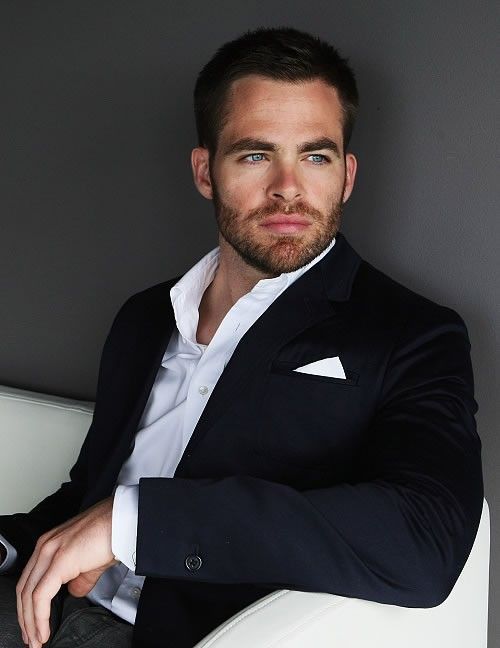 a man in a suit sitting on a white chair with his arms crossed and looking at the camera