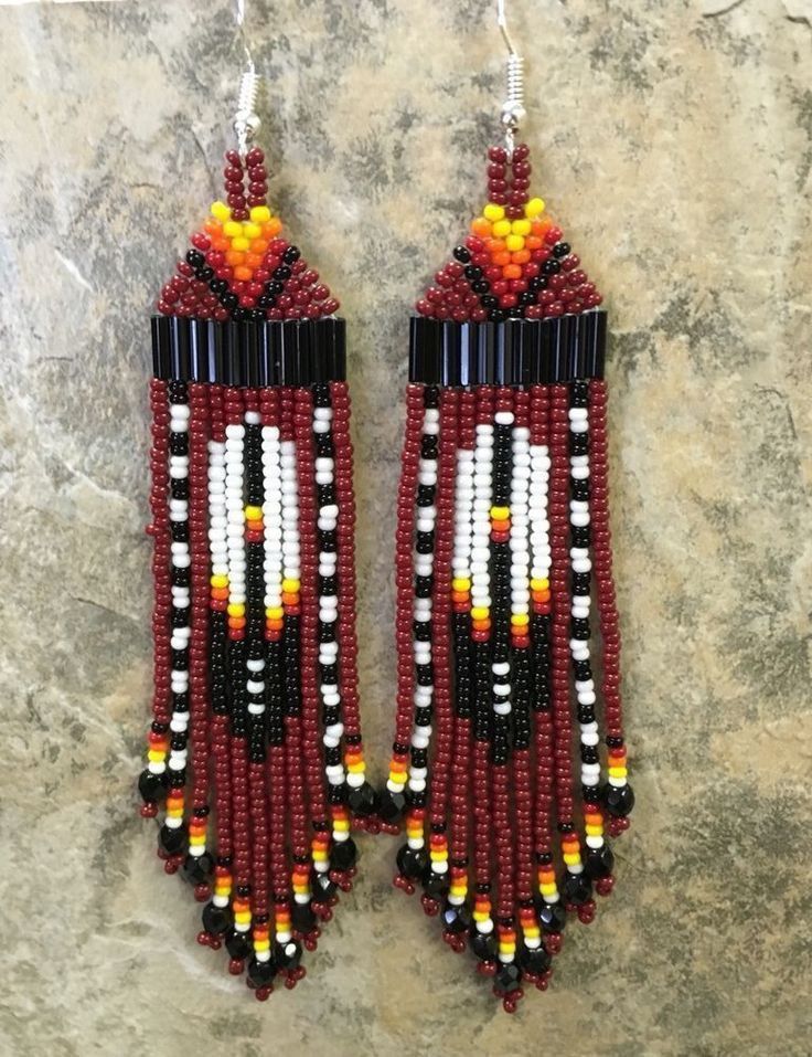 two red and white beaded earrings on a rock wall, with beads hanging from them