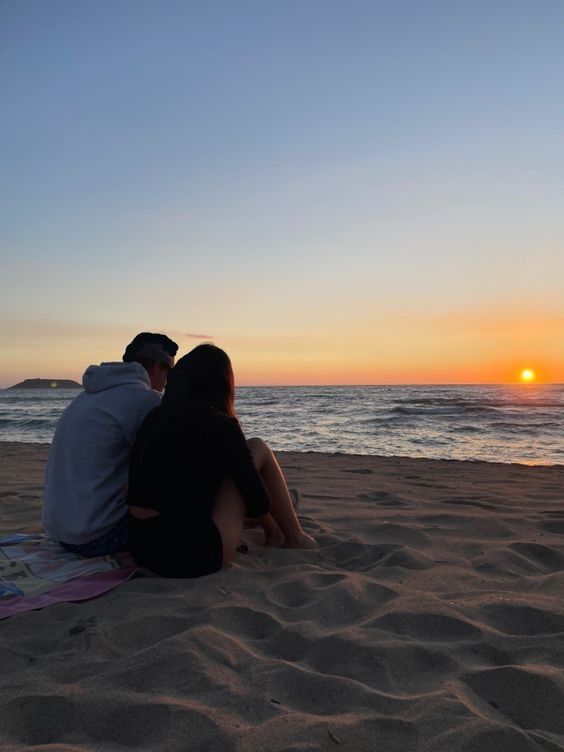 two people sitting on the beach watching the sunset