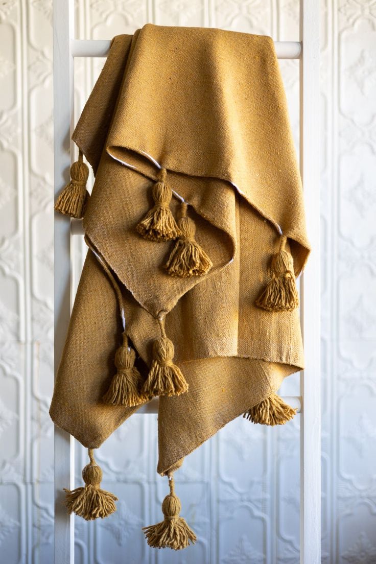 three towels hanging on a ladder with tassels in front of a white wall