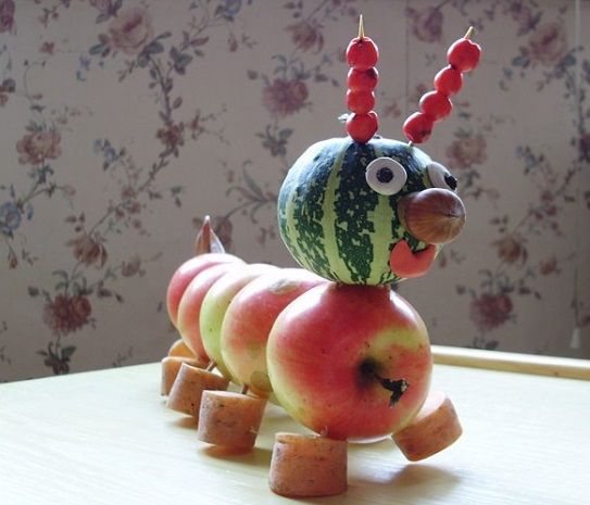 an apple and watermelon caterpillar sculpture sitting on top of a table