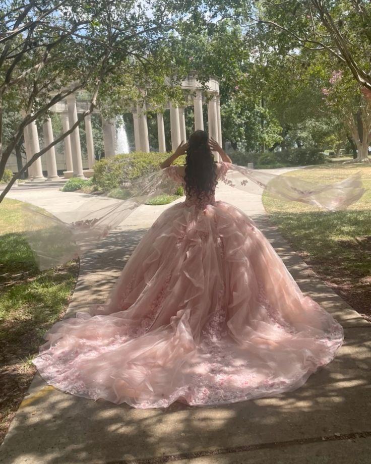 a woman in a pink dress is sitting on the ground near some trees and columns