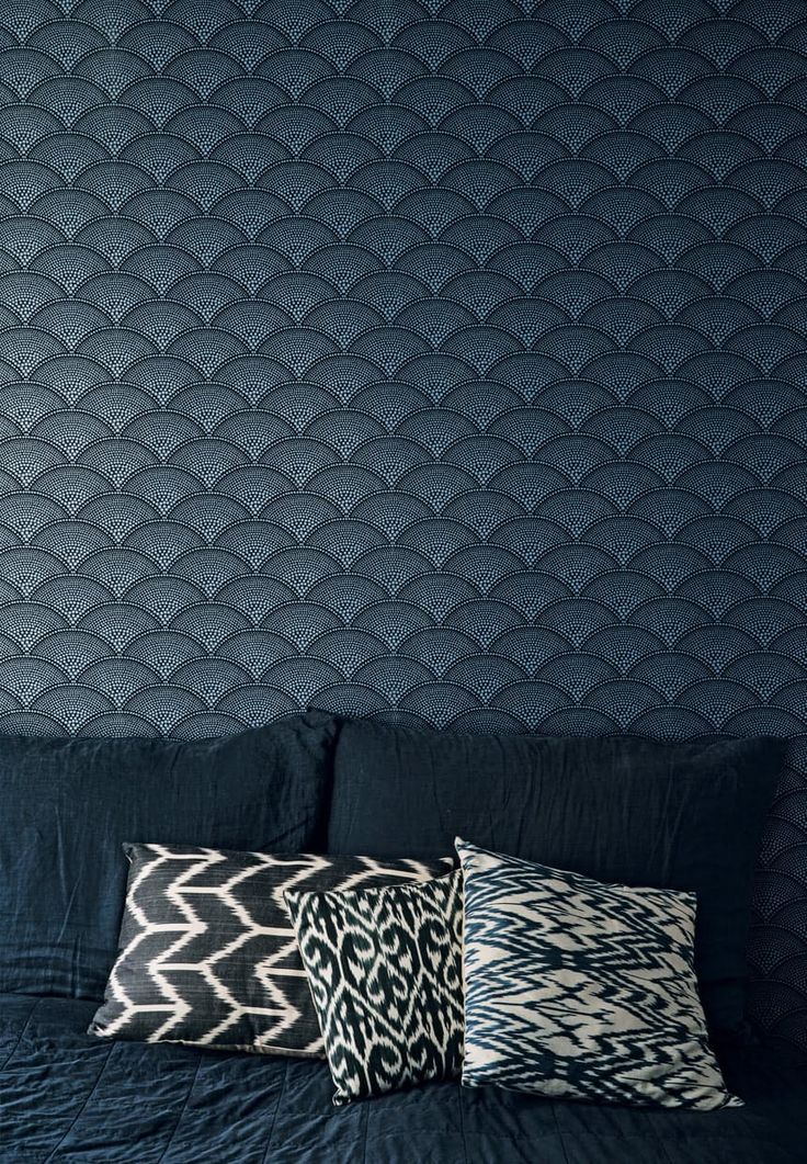 three pillows are sitting on a bed in front of a blue wall with wavy waves