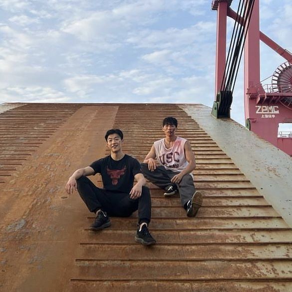 two young men sitting on the side of a metal stair case in front of a windmill