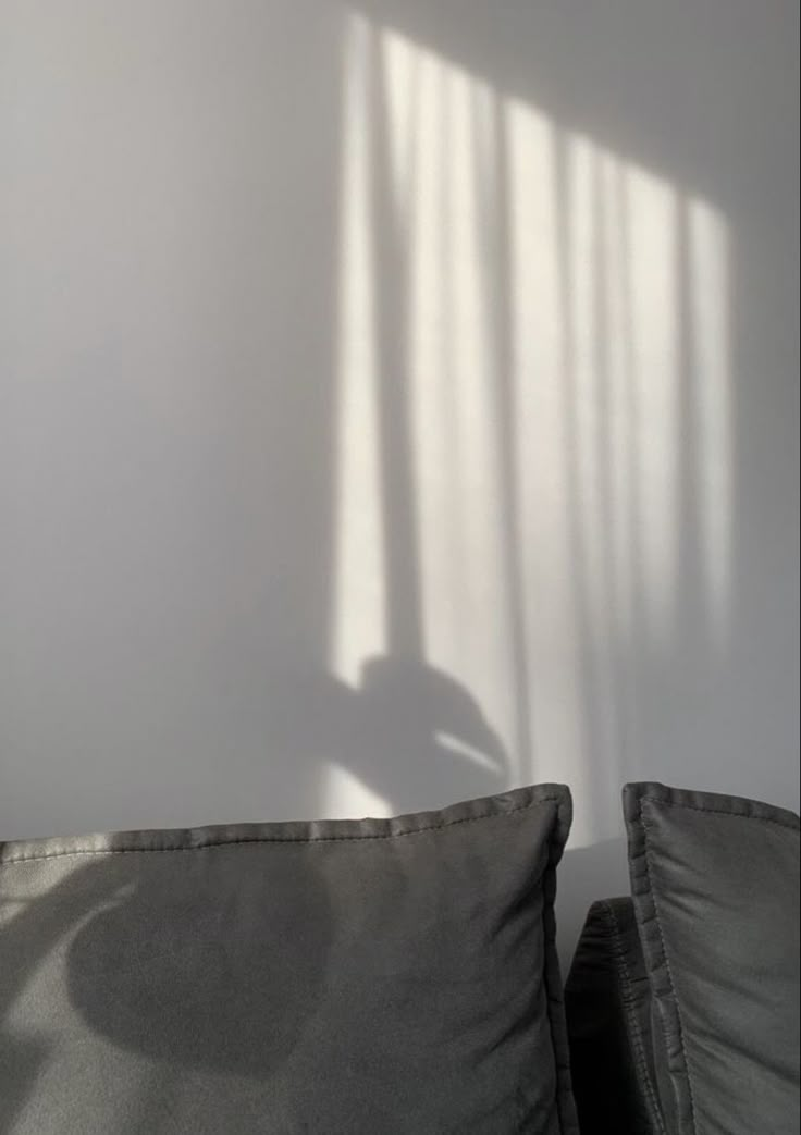 the shadow of a chair against a white wall in front of a gray couch with two pillows