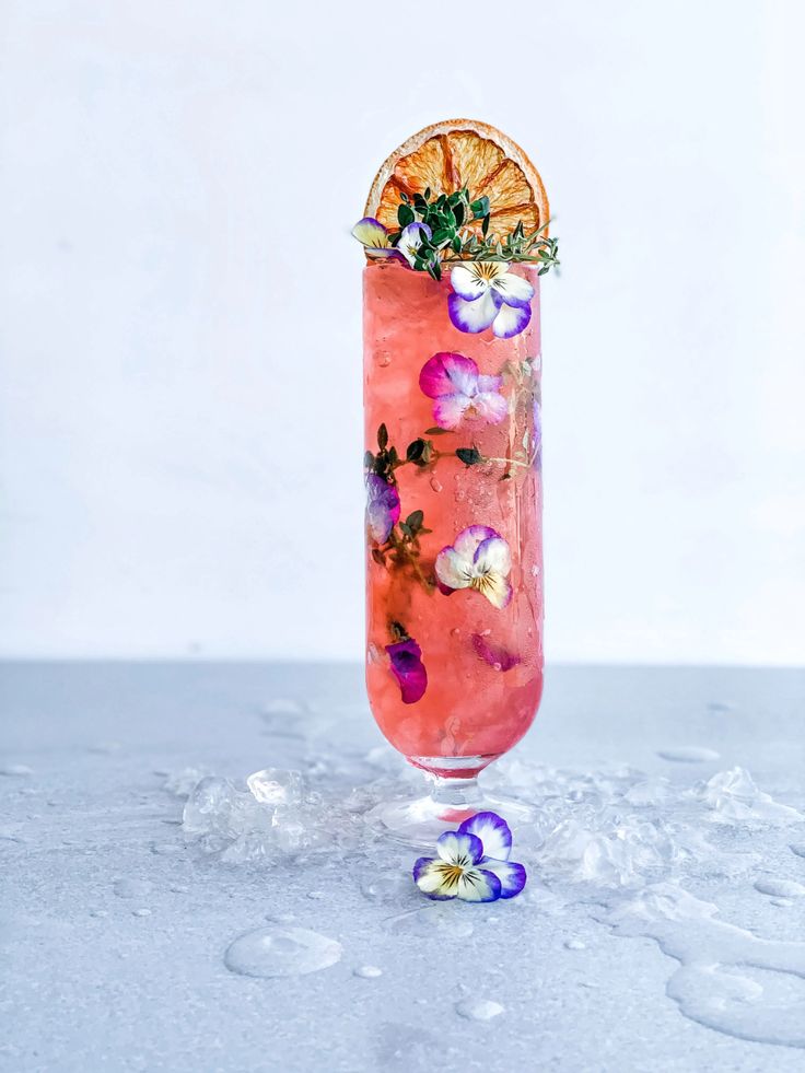 a tall glass filled with pink liquid and garnished with flowers on the rim