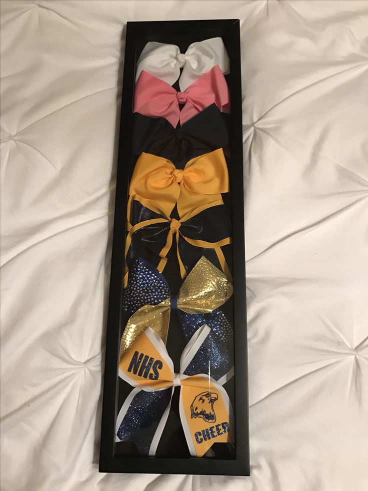 three bow ties in a black box on a white sheet with gold and pink bows