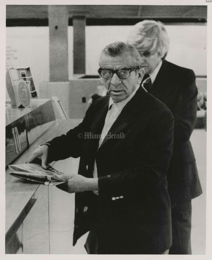 black and white photograph of two men looking at something on the counter in front of them