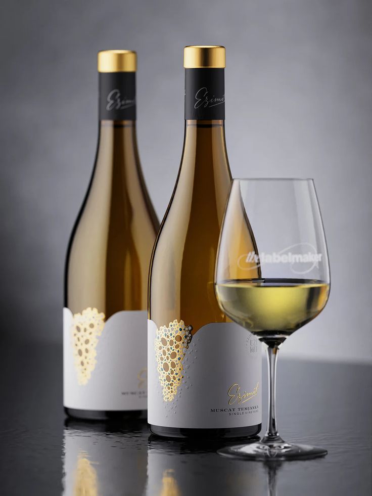 three bottles and two glasses of white wine on a table with a gray back ground