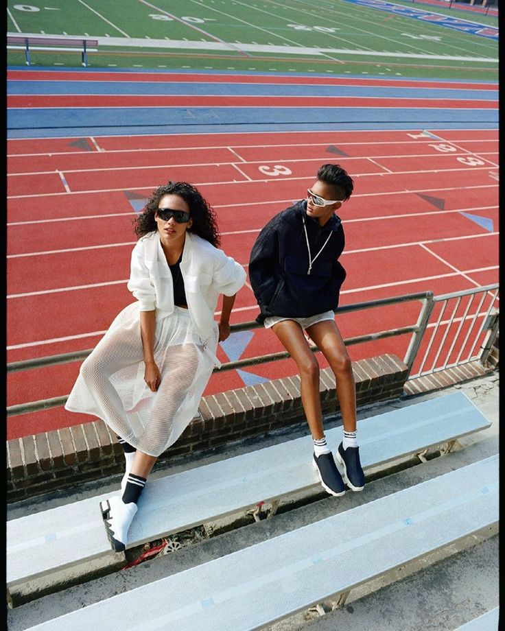 two young women sitting on the bleachers at a sports stadium, one wearing sunglasses