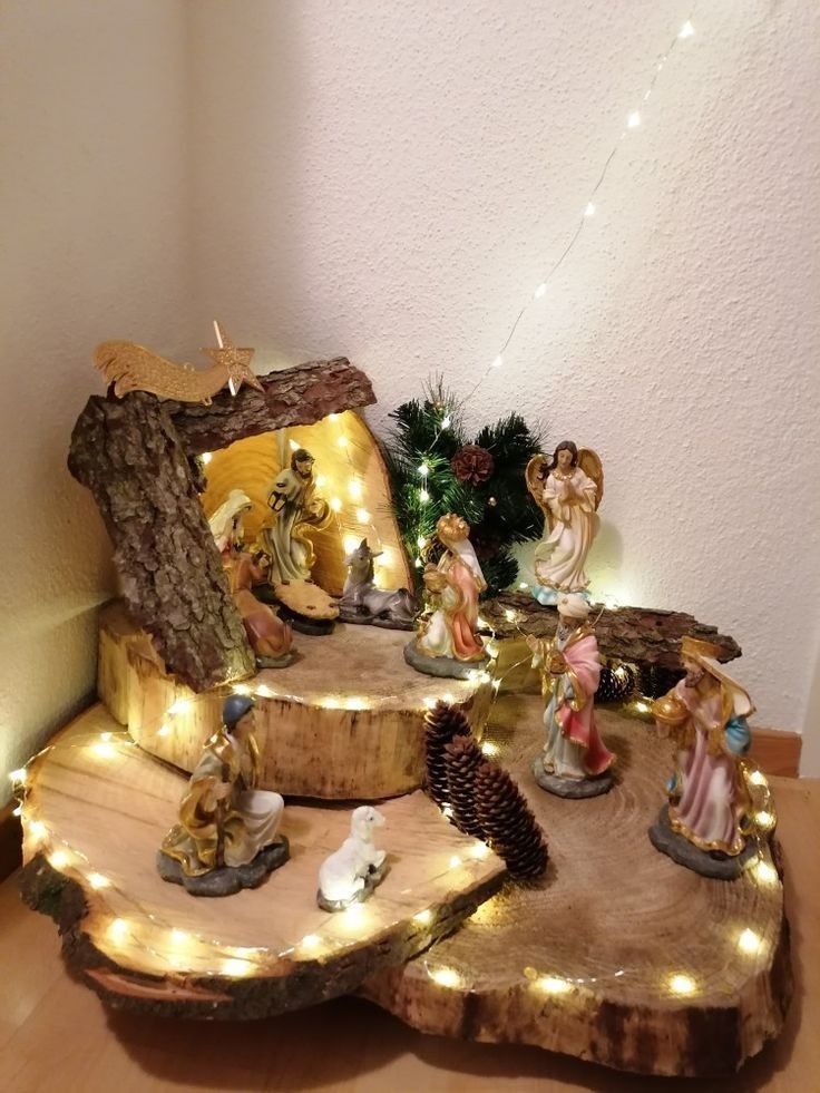 a nativity scene with figurines and lights on a tree stump in front of a white wall