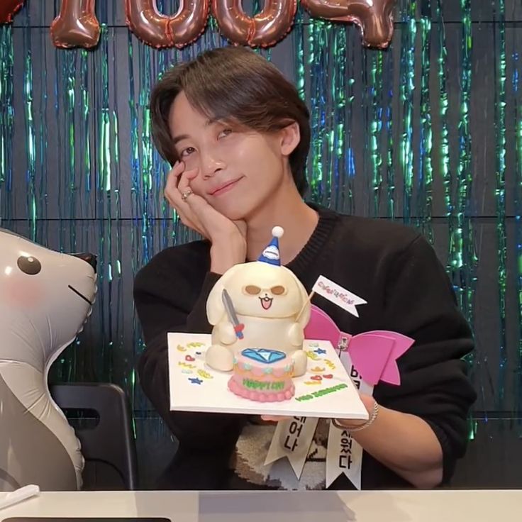 a young man holding a cake in front of a balloon wall with the word boo on it