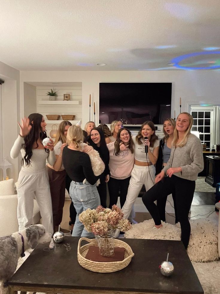 a group of young women standing around a living room with their arms in the air