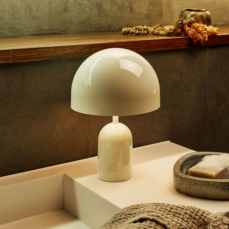 a white table lamp sitting on top of a counter next to a bowl and towel