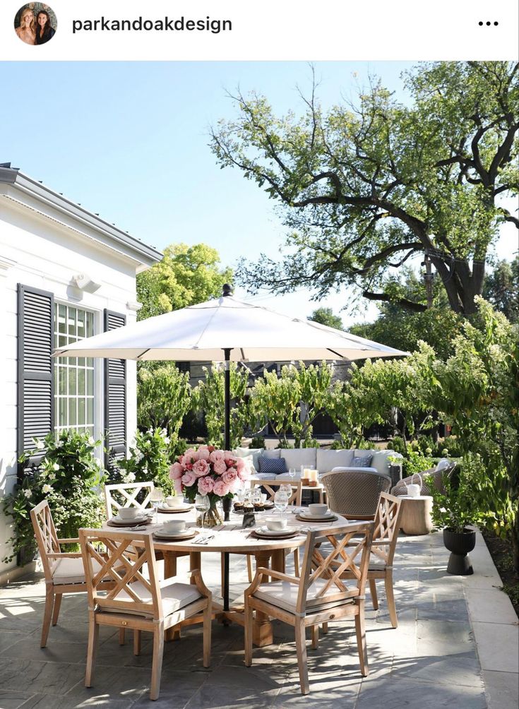 an outdoor dining table and chairs with umbrellas on the back patio, surrounded by greenery