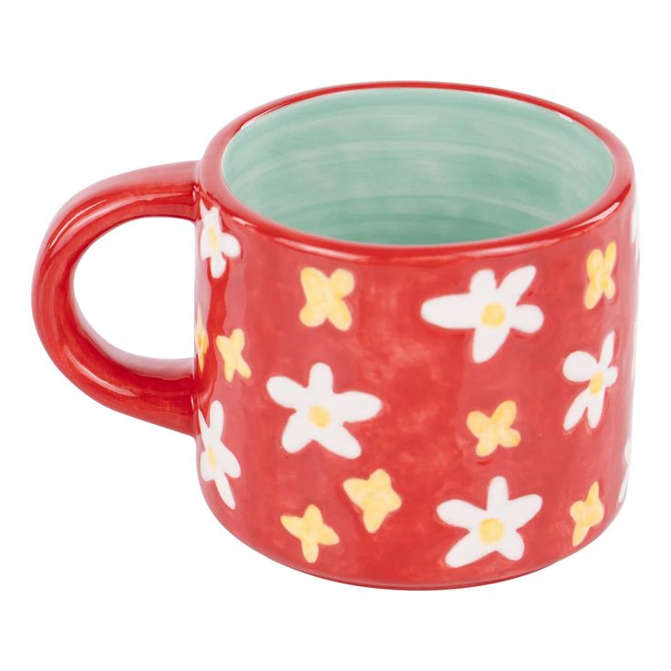 a red mug with yellow and white flowers on it's side, sitting in front of a white background