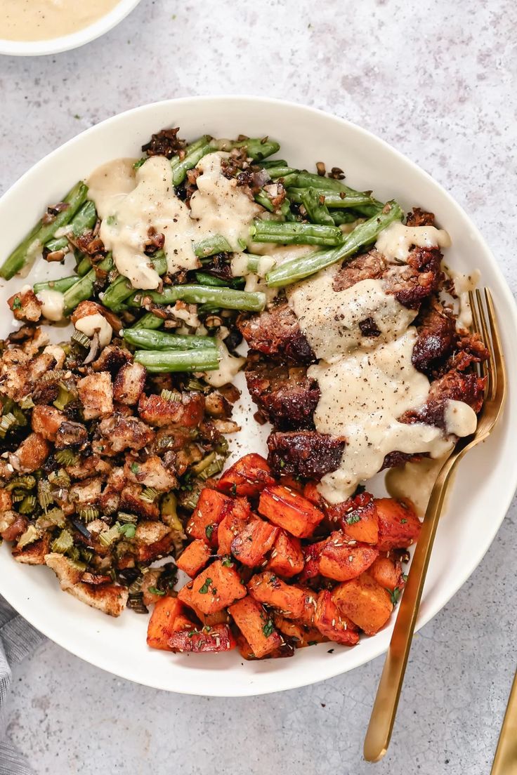 a white plate topped with meat and veggies next to a bowl of gravy