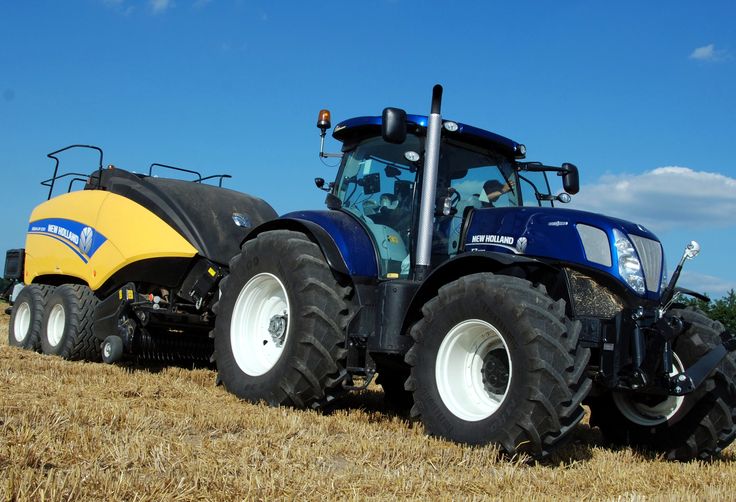 a blue tractor pulling a yellow trailer behind it on top of a dry grass field