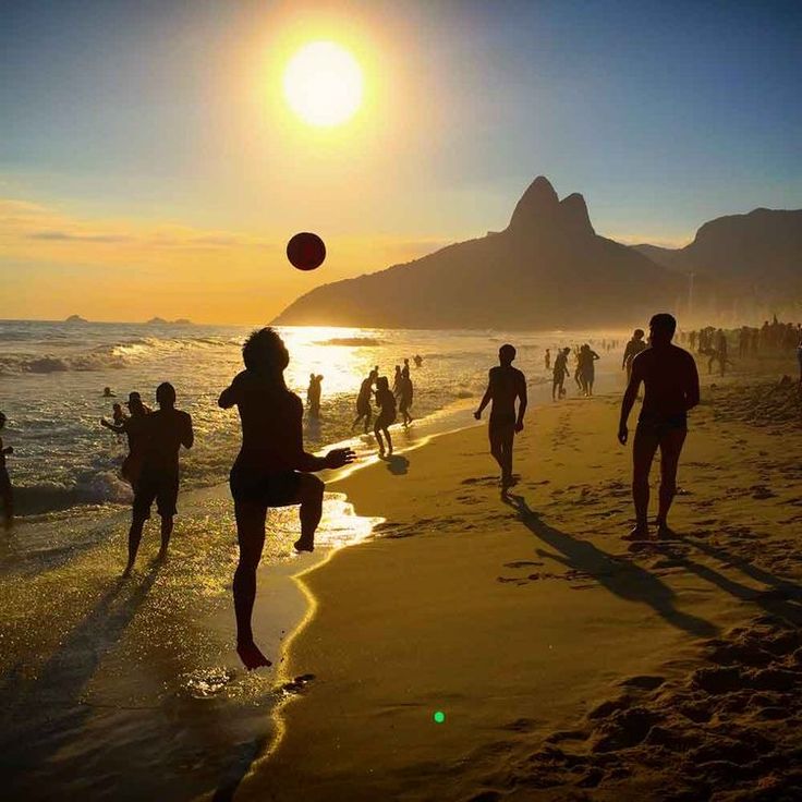 people are playing with a ball on the beach at sunset, while others run and play in the water