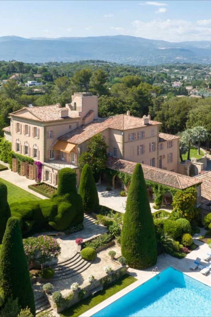 an aerial view of a mansion with a pool in the foreground and trees surrounding it