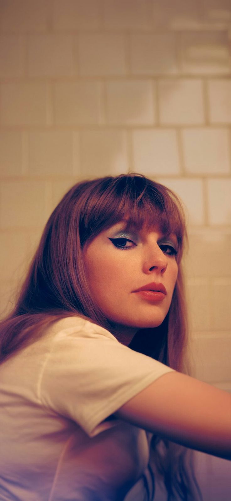 a woman with long red hair and blue eyes is looking at her cell phone while leaning against a brick wall