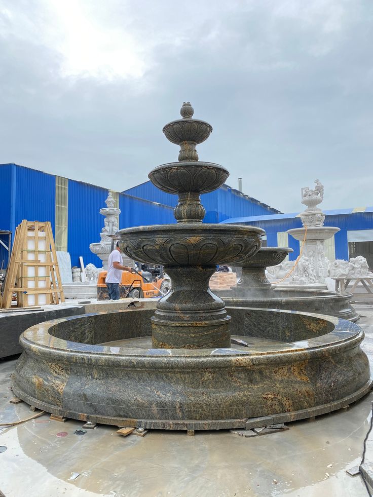 an outdoor fountain in front of a blue building with workers working on the back wall