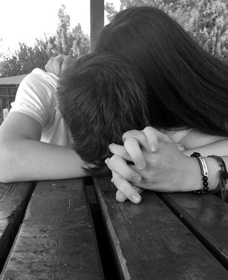 a man and woman sitting on top of a wooden picnic table next to each other