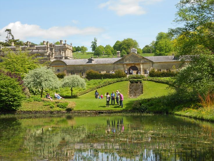 people are standing on the bank of a pond in front of a large building with many windows