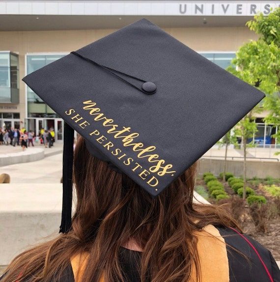 a woman wearing a black graduation cap with gold lettering on it's side and her hair in the wind