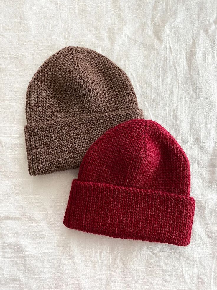 two knitted hats laying on top of a white bed sheet next to each other