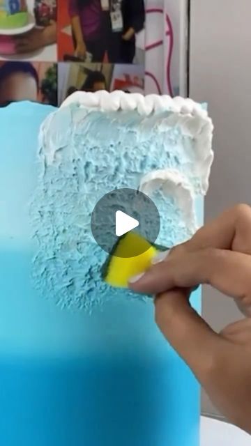 someone is decorating a blue cake with white frosting and yellow decorations on it