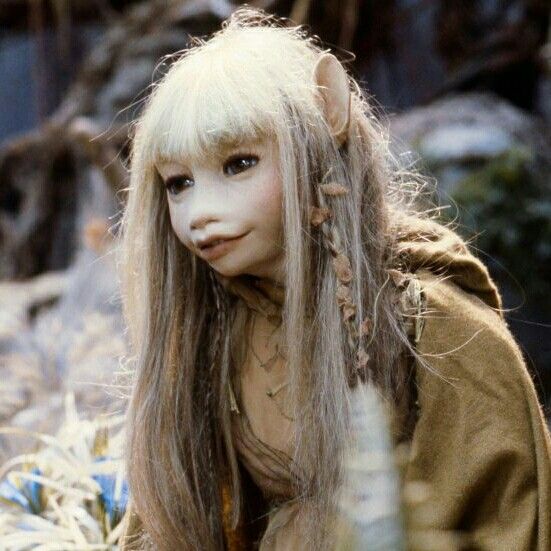 a woman with long hair and white skin is standing in tall grass, looking at the camera