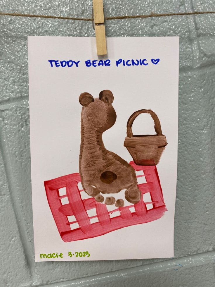 a drawing of a giraffe with a basket hanging on a clothesline that says teddy bear picnic