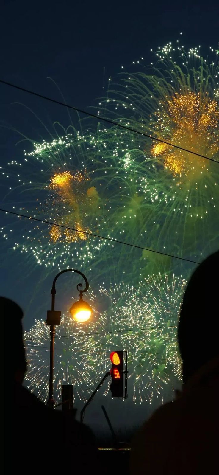 fireworks are lit up in the night sky above a street light and traffic signal as people watch