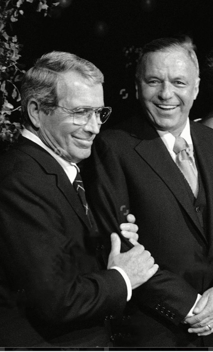 black and white photograph of three men in suits smiling at the camera with one holding his arm around another man's shoulder