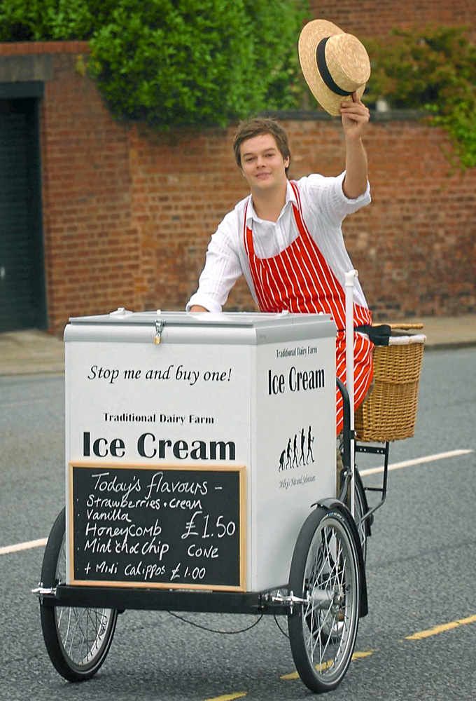 a man in an ice cream cart waving to the camera while holding a straw hat