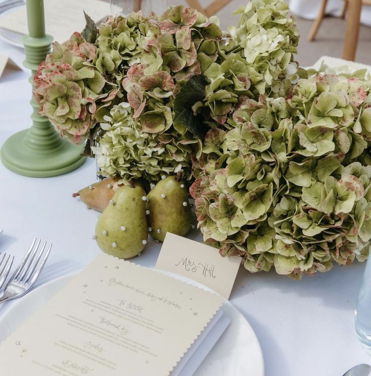 the table is set with flowers, pears and menu cards for an elegant dinner