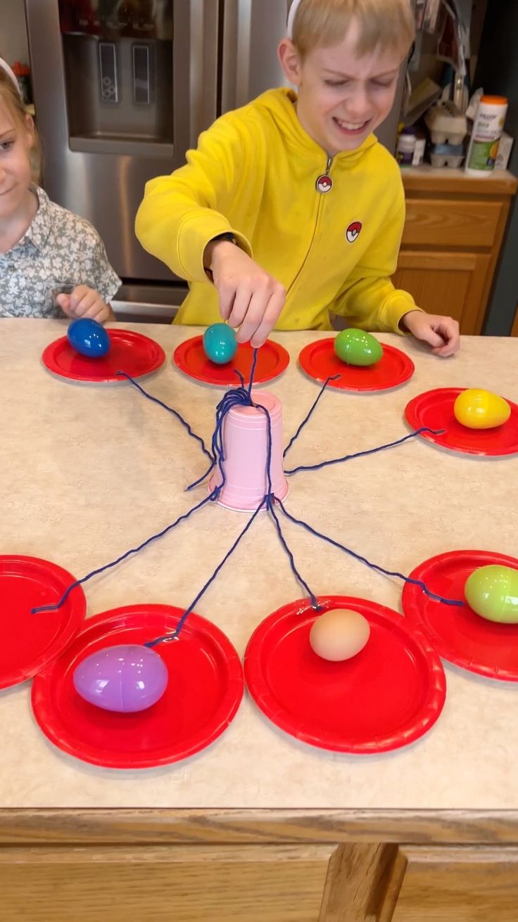 two children are playing with paper plates on the kitchen counter and one child is holding an easter egg