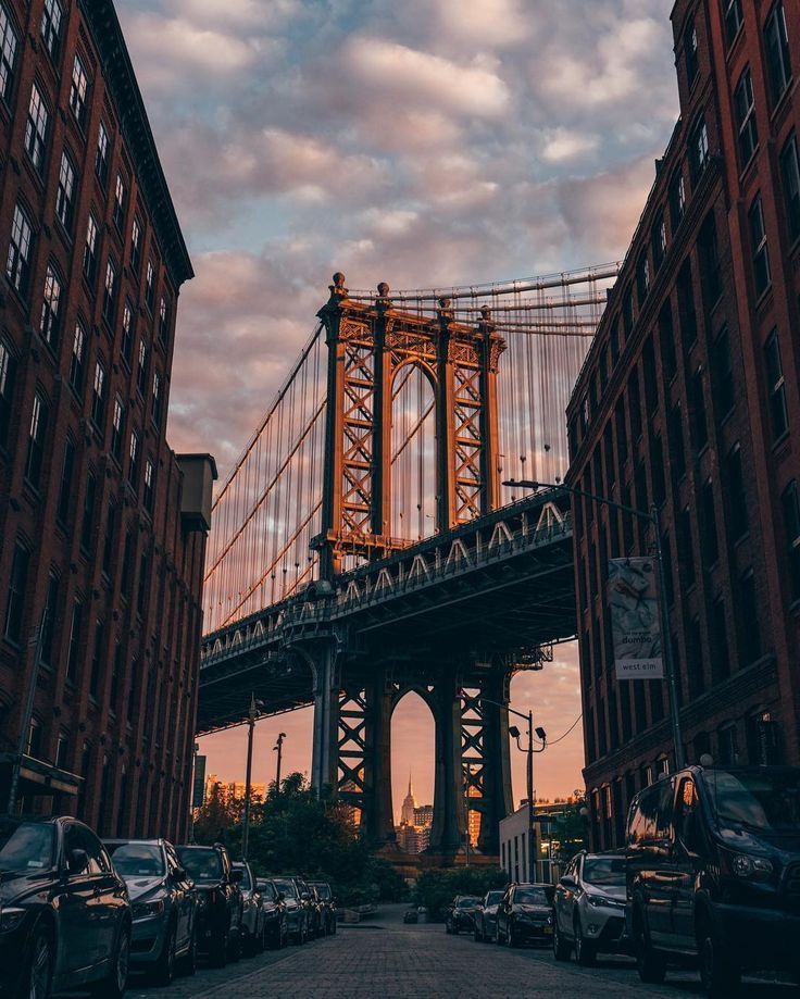 cars are parked in front of tall buildings and the bridge is lit up at sunset