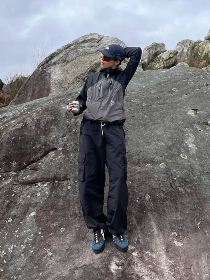 a man standing on top of a large rock with his hands in the air while wearing blue shoes